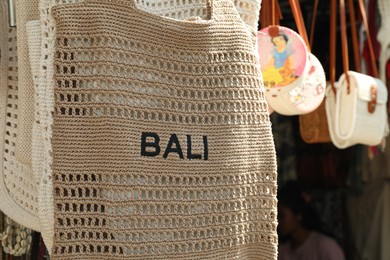 Photo of Bali, Indonesia - May 25, 2025: Beige knitted bag with word and other souvenirs at outdoor market, closeup