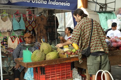 Photo of Bali, Indonesia - May 25, 2025: Tourist buying exotic fruits at outdoor market