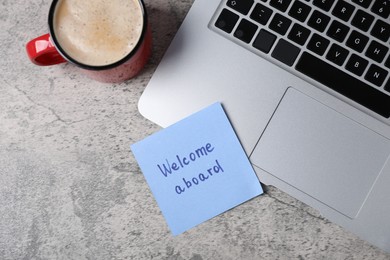 Photo of Sticky note with phrase Welcome Aboard, laptop and coffee on grey table, flat lay