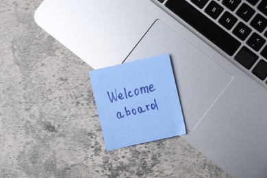 Photo of Sticky note with phrase Welcome Aboard and laptop on grey table, top view