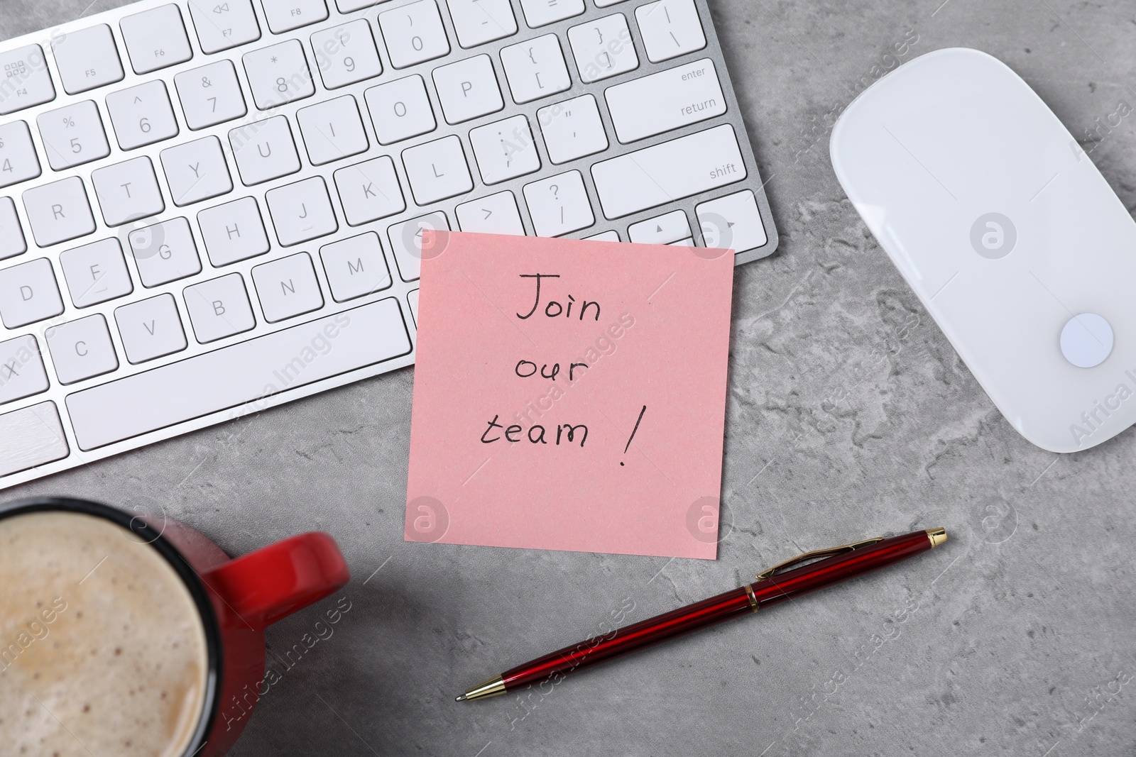Photo of Sticky note with phrase Join Our Team, keyboard, mouse, pen and coffee on grey table, flat lay