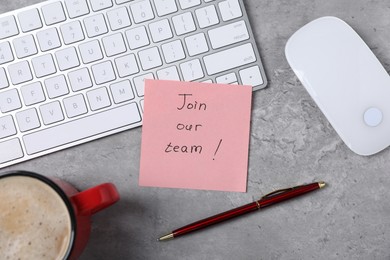 Photo of Sticky note with phrase Join Our Team, keyboard, mouse, pen and coffee on grey table, flat lay