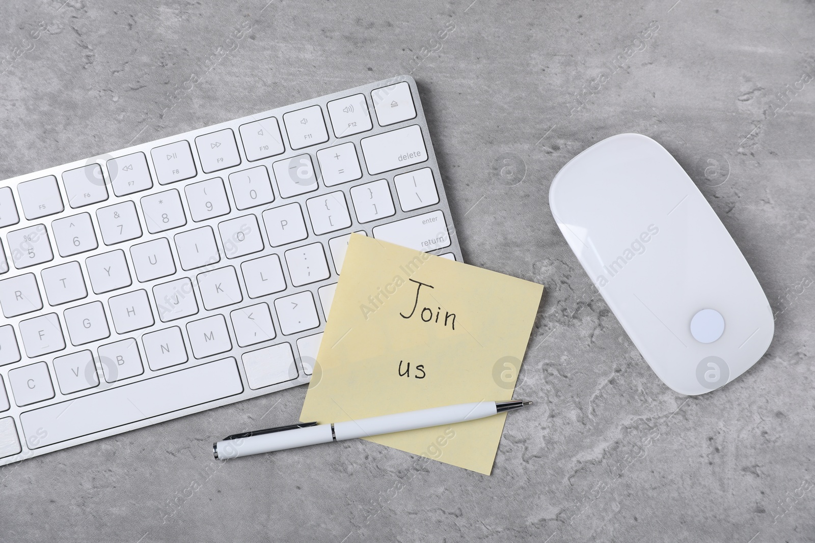 Photo of Sticky note with phrase Join Us, computer keyboard, mouse and pen on grey table, flat lay