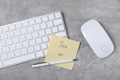 Photo of Sticky note with phrase Join Us, computer keyboard, mouse and pen on grey table, flat lay