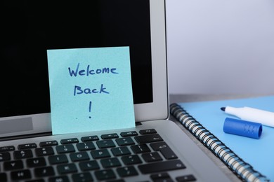 Photo of Sticky note with phrase Welcome Back, laptop, marker and notebook on table, closeup
