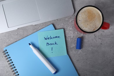 Photo of Sticky note with phrase Welcome Back, laptop, coffee, marker and notebook on grey table, flat lay
