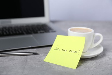 Photo of Sticky note with phrase Join Our Team, coffee, pen and laptop on grey table, closeup