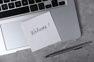 Photo of Sticky note with word Welcome, pen and laptop on grey table, flat lay