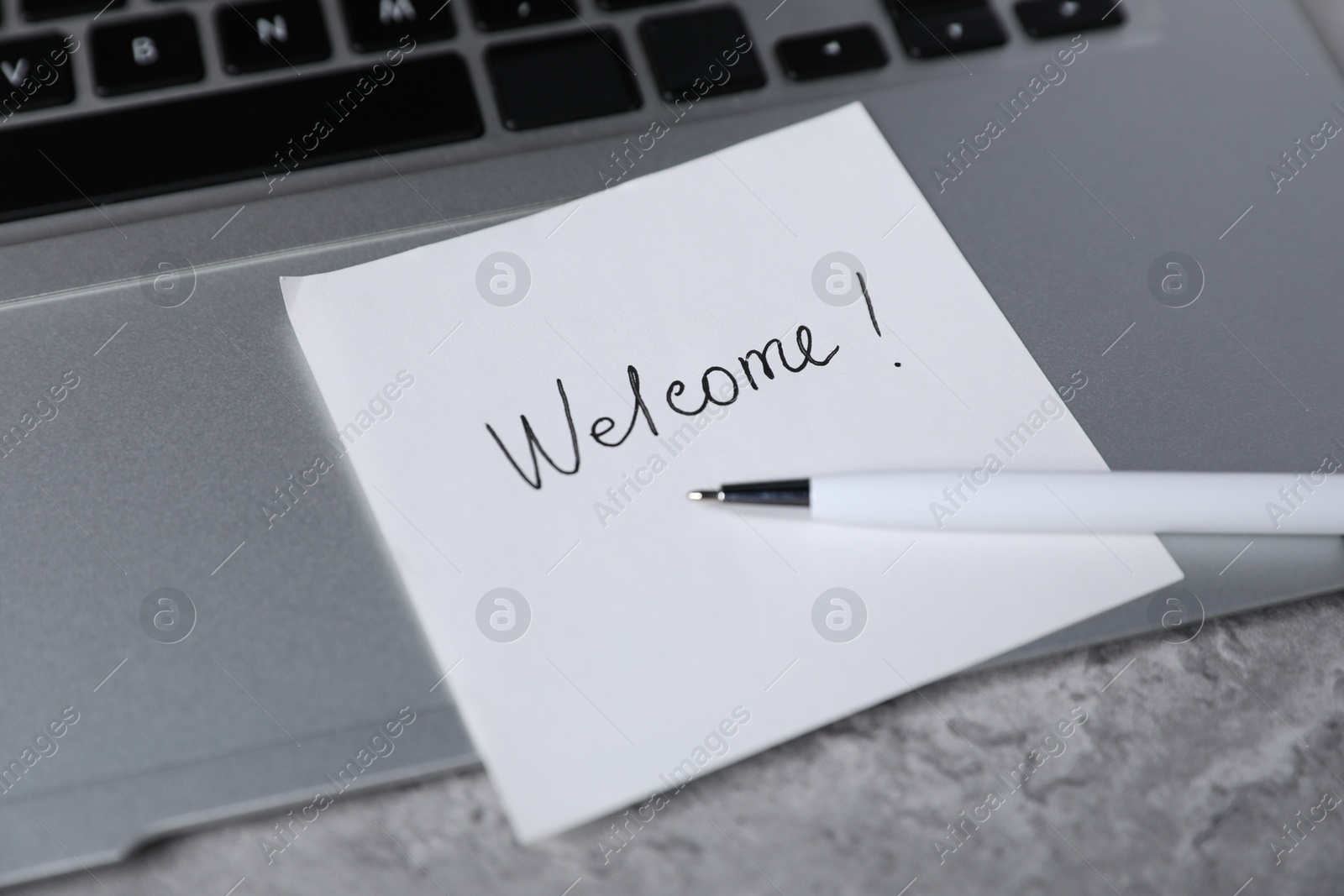 Sticky note with word Welcome, pen and laptop on grey table, closeup Photo of Sticky note with word Welcome, pen and laptop on grey table, closeup