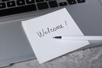 Photo of Sticky note with word Welcome, pen and laptop on grey table, closeup