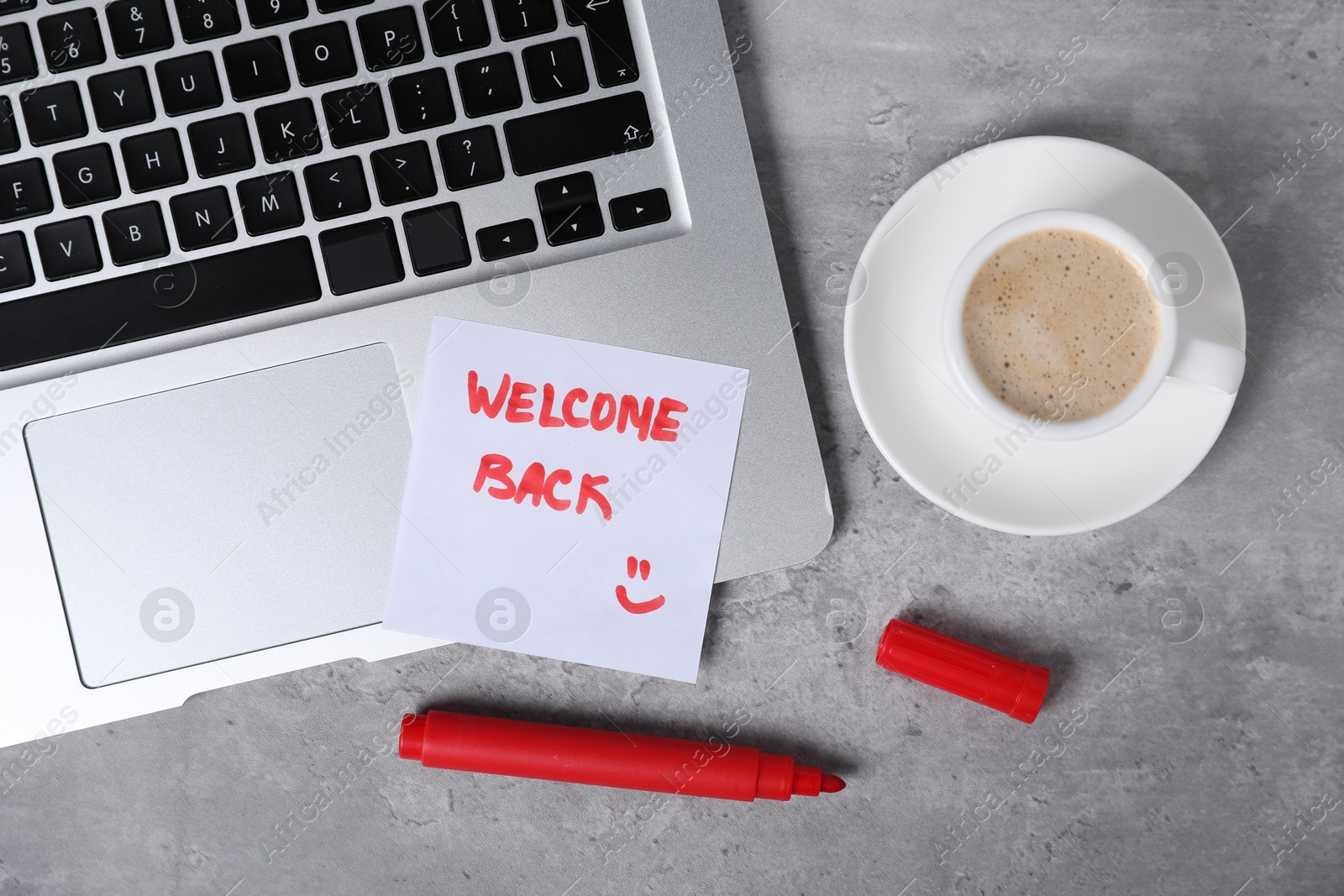 Sticky note with phrase Welcome Back, coffee, marker and laptop on grey table, flat lay Photo of Sticky note with phrase Welcome Back, coffee, marker and laptop on grey table, flat lay