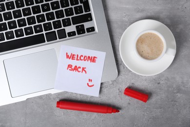 Photo of Sticky note with phrase Welcome Back, coffee, marker and laptop on grey table, flat lay