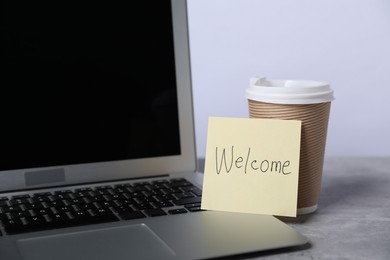 Photo of Sticky note with word Welcome, coffee and laptop on grey table, closeup