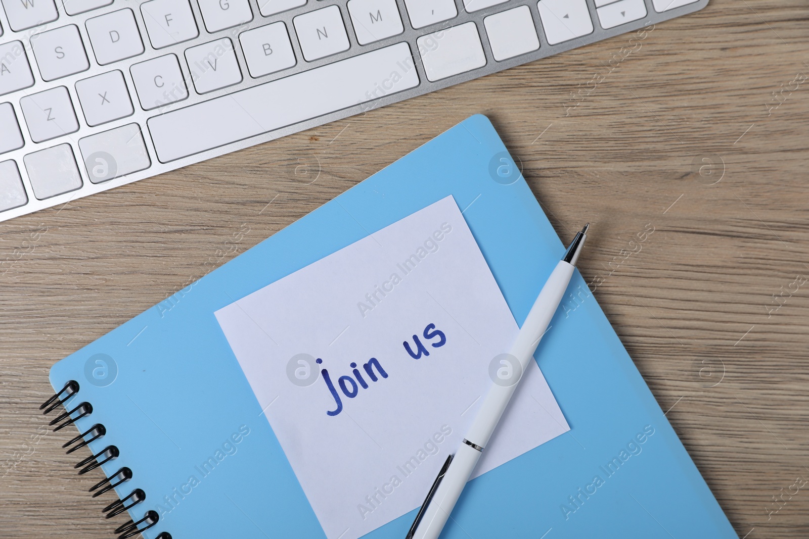 Sticky note with phrase Join Us, pen, notebook and computer keyboard on wooden table, flat lay Photo of Sticky note with phrase Join Us, pen, notebook and computer keyboard on wooden table, flat lay
