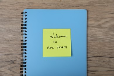 Photo of Sticky note with phrase Welcome To The Team and notebook on wooden table, top view