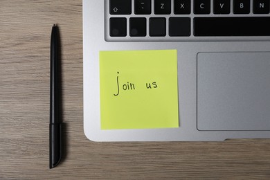Photo of Sticky note with phrase Join Us, laptop and marker on wooden table, flat lay