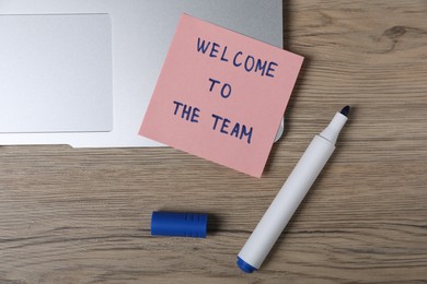 Photo of Sticky note with phrase Welcome To The Team, marker and laptop on wooden table, flat lay