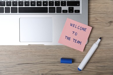 Photo of Sticky note with phrase Welcome To The Team, marker and laptop on wooden table, flat lay