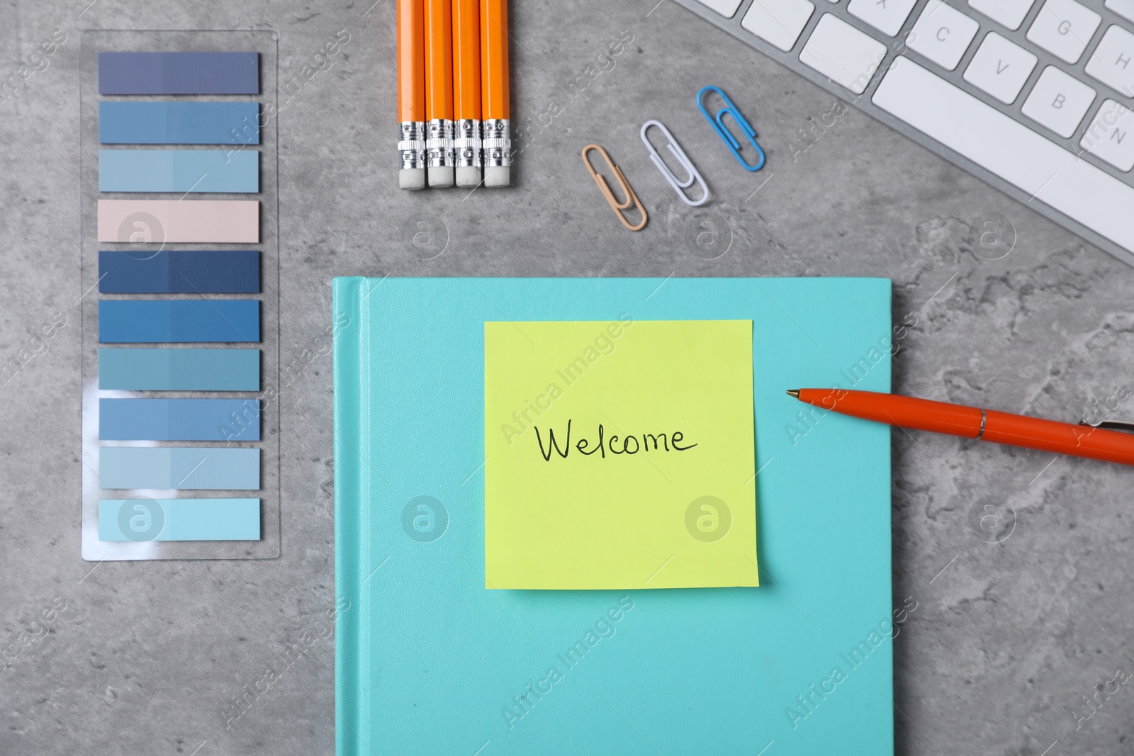 Sticky note with word Welcome, stationery and keyboard on grey table, flat lay Photo of Sticky note with word Welcome, stationery and keyboard on grey table, flat lay