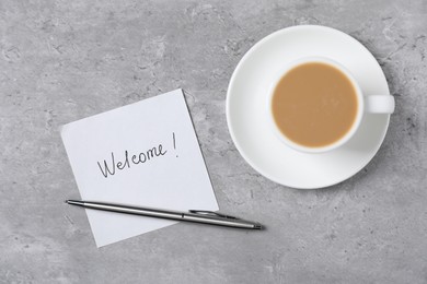 Photo of Sticky note with word Welcome, coffee and pen on grey table, flat lay
