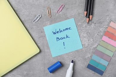 Photo of Sticky note with phrase Welcome Back and different stationery on grey table, flat lay