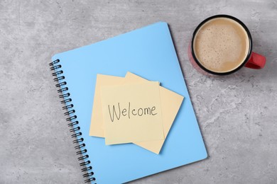 Photo of Sticky note with word Welcome, notebook and coffee on grey table, flat lay