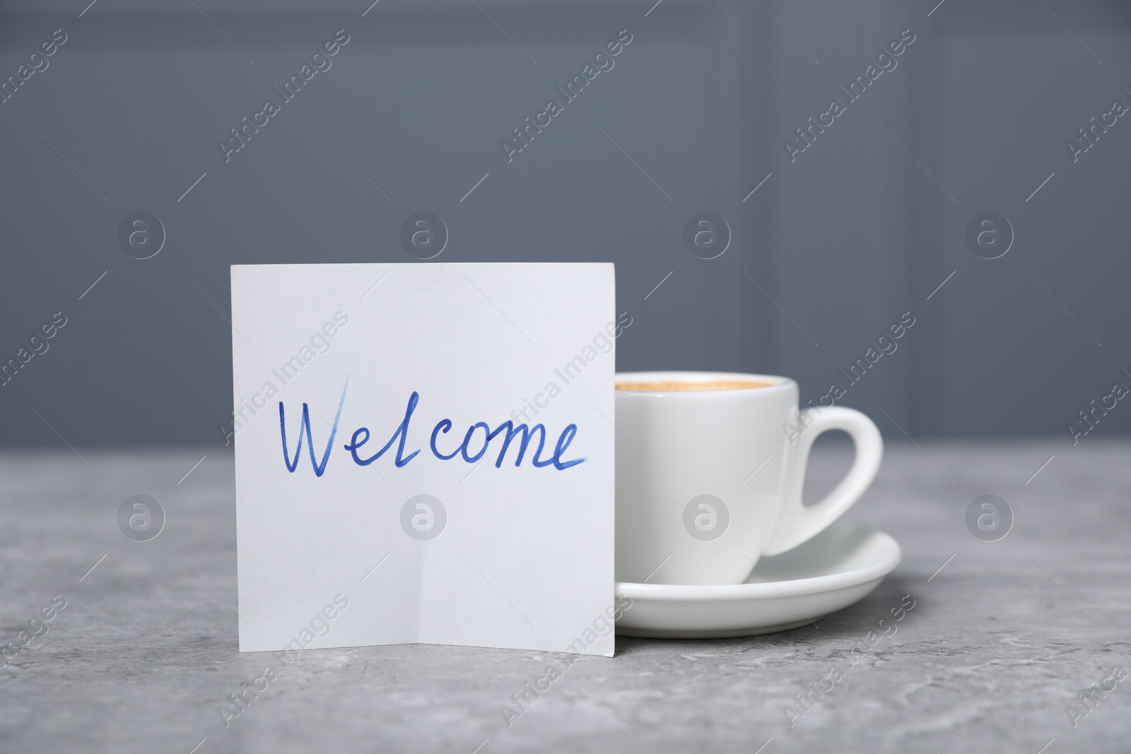 Sticky note with word Welcome and coffee on grey table, closeup Photo of Sticky note with word Welcome and coffee on grey table, closeup