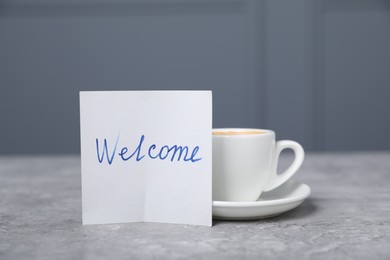 Photo of Sticky note with word Welcome and coffee on grey table, closeup
