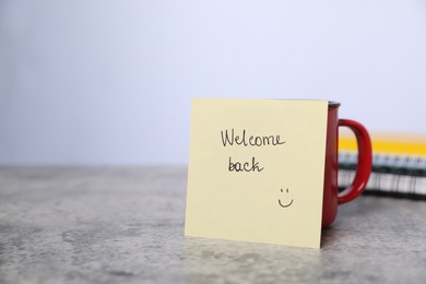 Photo of Sticky note with phrase Welcome Back and coffee on grey table, closeup. Space for text