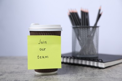 Photo of Sticky note with phrase Join Our Team, coffee, notebook and pencils on grey table, closeup