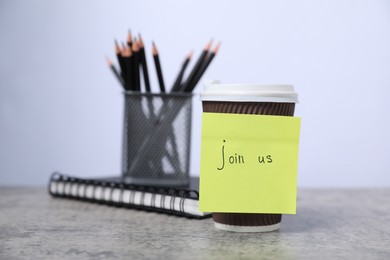 Photo of Sticky note with phrase Join Us, coffee, notebook and pencils on grey table