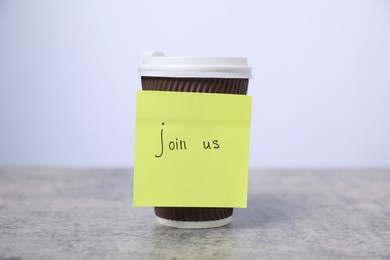 Photo of Sticky note with phrase Join Us and coffee on grey table, closeup