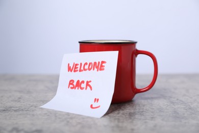 Photo of Sticky note with phrase Welcome Back and coffee on grey table, closeup