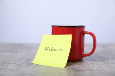 Photo of Sticky note with word Welcome and coffee on grey table, closeup