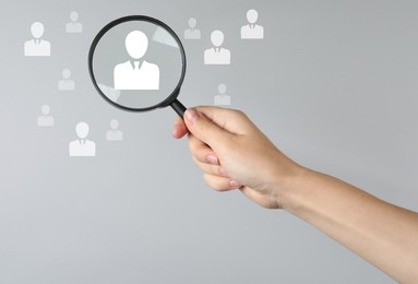 Image of Employee search. HR manager holding magnifying glass over human icons against grey background, closeup