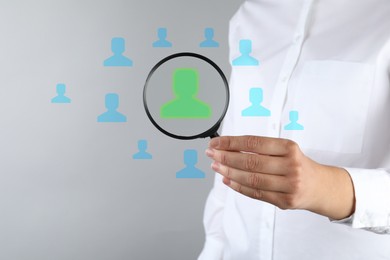 Image of Employee search. HR manager holding magnifying glass over human icons against grey background, closeup