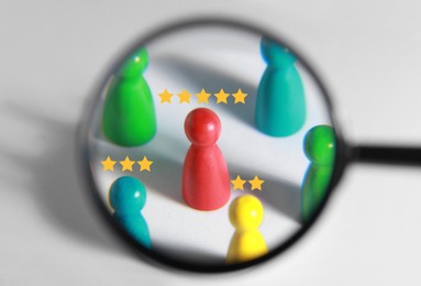 Image of Employee search. Different colorful pawns with stars on white background, view through magnifying glass