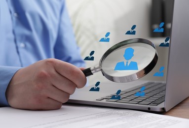 Image of Employee search. Man holding magnifier near laptop at wooden table, closeup. Human icons as candidates