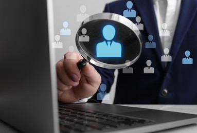 Image of Employee search. Man holding magnifier near laptop at wooden table, closeup. Human icons as candidates