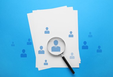 Image of Employee search. Sheets of paper, human icons and magnifying glass on light blue background, top view