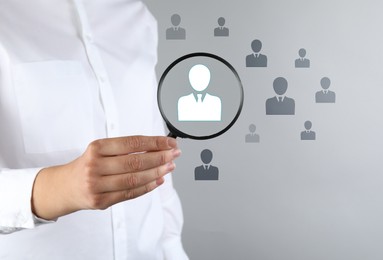Image of Employee search. HR manager holding magnifying glass over human icons against grey background, closeup