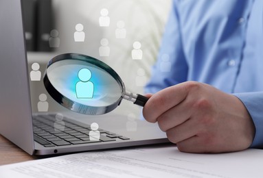 Image of Employee search. Man holding magnifier near laptop at wooden table, closeup. Human icons as candidates