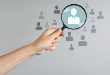 Image of Employee search. HR manager holding magnifying glass over human icons against grey background, closeup