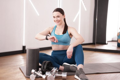 Photo of Woman checking fitness tracker during training indoors