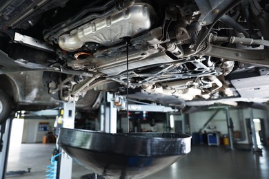 Photo of Dirty old motor oil dripping from car engine into container in workshop, closeup