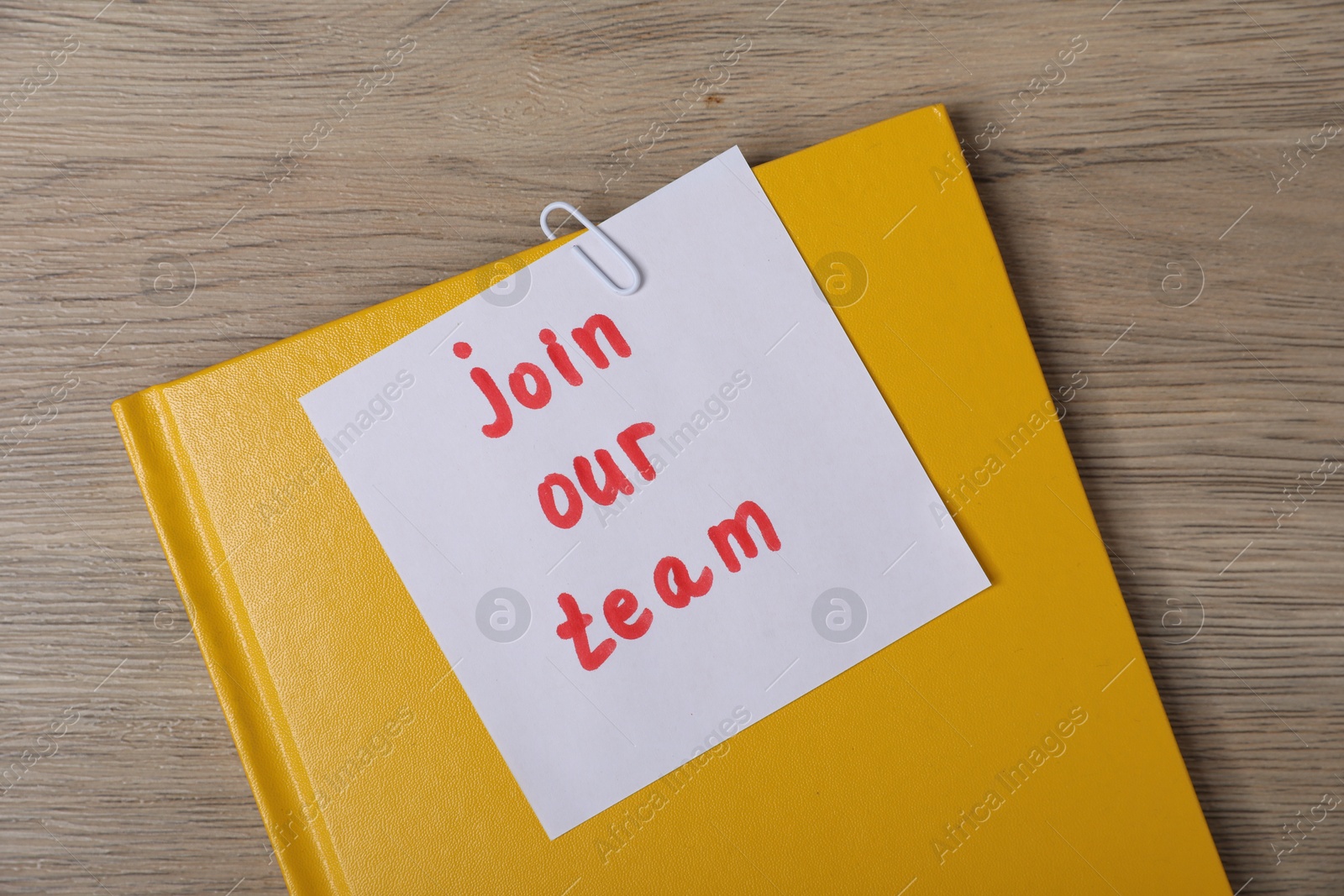 Sticky note with phrase Join Our Team and notebook on wooden table, top view Photo of Sticky note with phrase Join Our Team and notebook on wooden table, top view