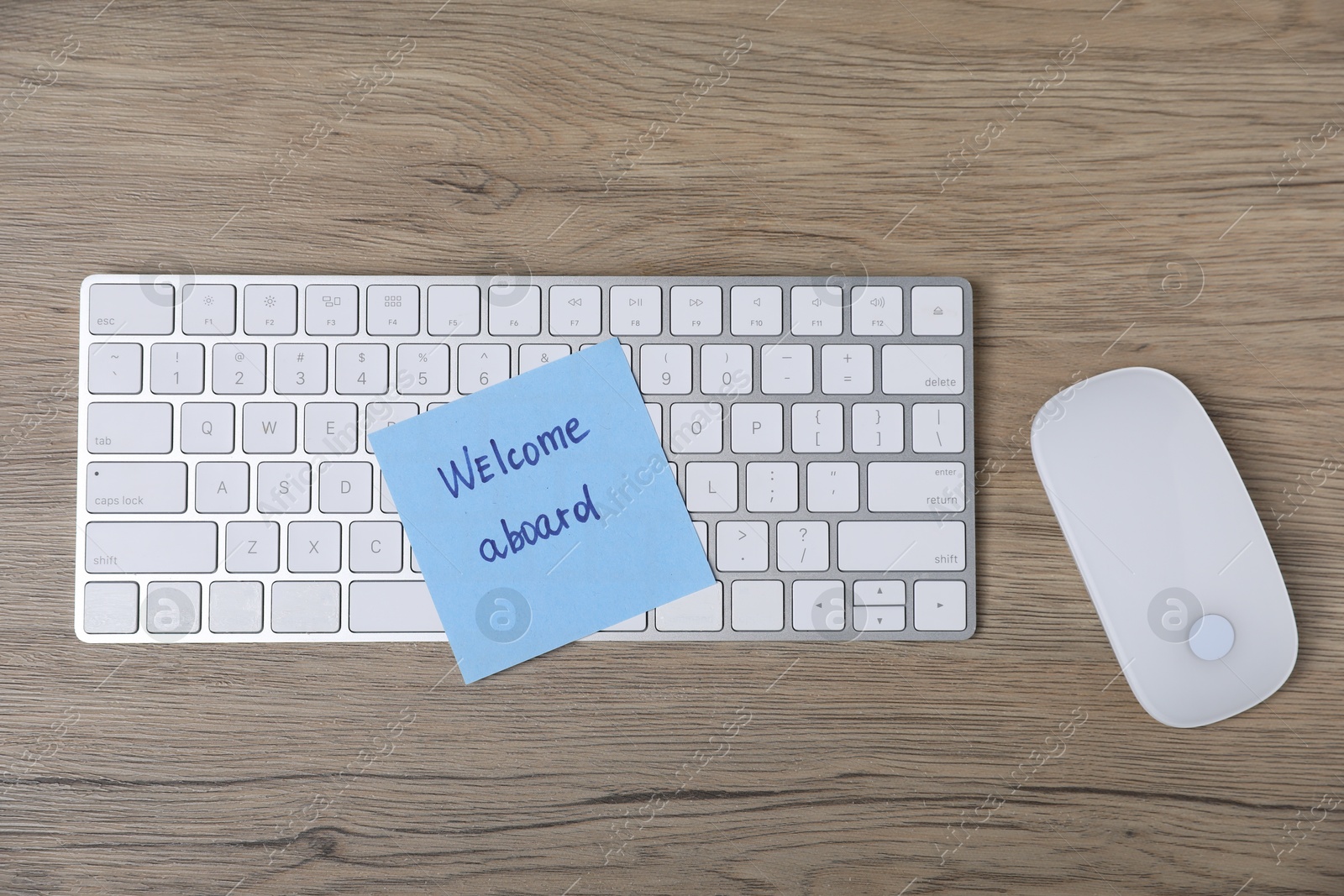 Sticky note with phrase Welcome Aboard, computer keyboard and mouse on wooden table, flat lay Photo of Sticky note with phrase Welcome Aboard, computer keyboard and mouse on wooden table, flat lay