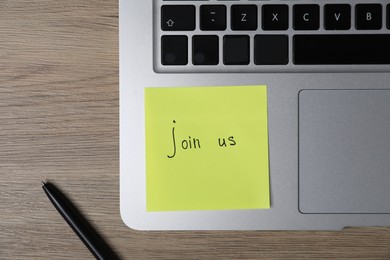 Photo of Sticky note with phrase Join Us, laptop and marker on wooden table, flat lay