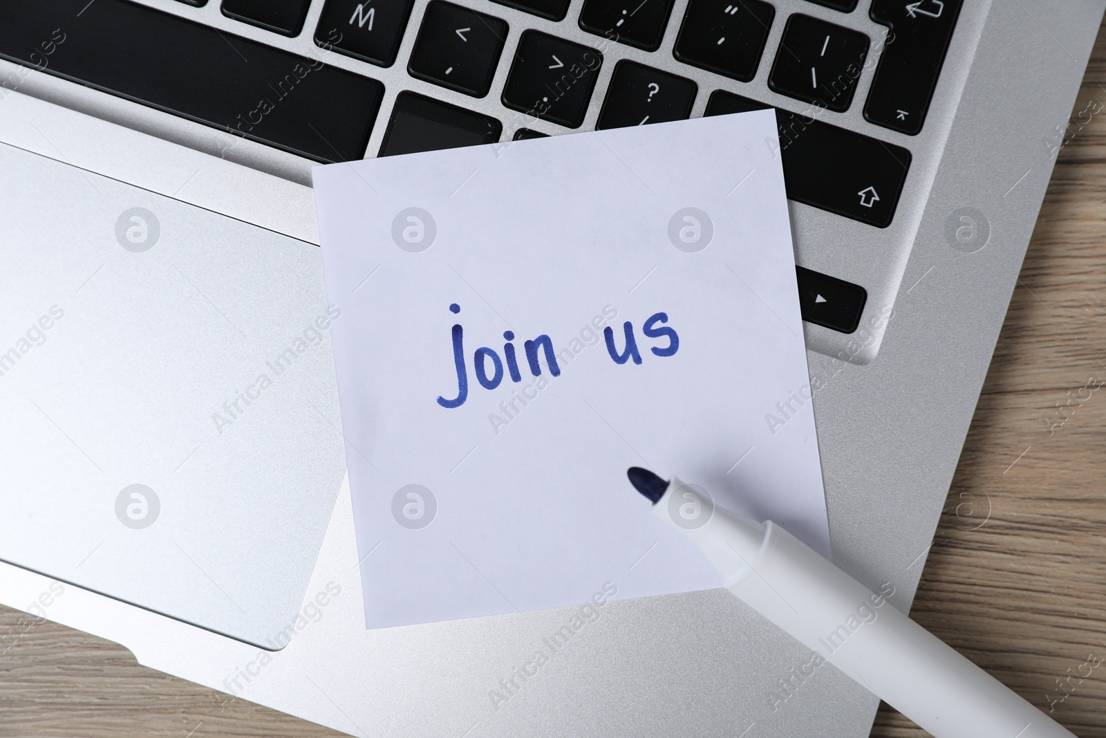 Sticky note with word Join Us, laptop and marker on wooden table, top view Photo of Sticky note with word Join Us, laptop and marker on wooden table, top view