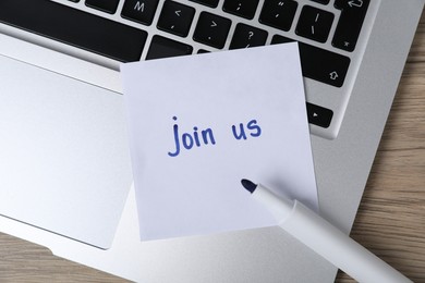 Photo of Sticky note with word Join Us, laptop and marker on wooden table, top view